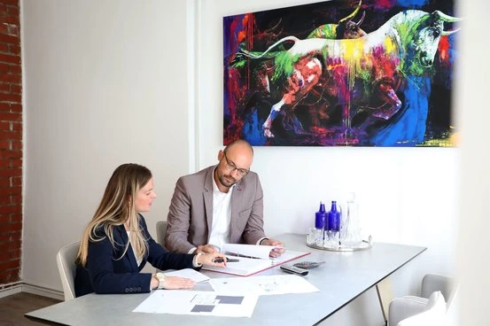 Zwei Personen besprechen Finanzunterlagen in modernem Büro mit farbigem Bullen-Gemälde.