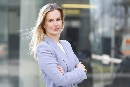 Geschäftsfrau mit blondem Haar im hellblauen Blazer steht selbstbewusst vor Bürogebäude.